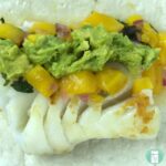 flour tortilla topped with white fish, guacamole, cubed mango