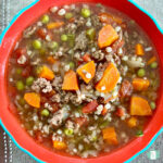 bowl of ground beef, carrots, peas, tomatoes, and barley in a broth