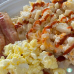 diced potatoes topped with ketchup next to bacon and scrambled eggs