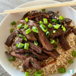 beef strips on rice topped with sliced green onions on a plate with chopsticks