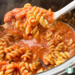 rotini pasta in a red sauce being scooped out of the slow cooker