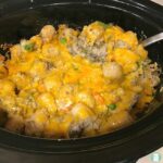 slow cooker with tater tots, ground beef, vegetables topped with shredded cheddar cheese