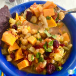 a spoon lifts a scoop out of a bowl of diced vegetables, chickpeas, and dried cranberries