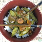 snow peas, carrots, and sauce on rice in a bowl with chopsticks