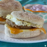 English muffin sandwich with sausage round, melted cheese slice, and cooked egg in it