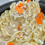 slow cooker with egg noodles, carrots, and shredded chicken