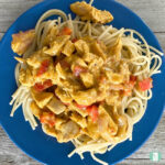 cubed chicken and diced red peppers in a creamy sauce on spaghetti noodles