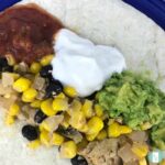 corn, black beans, diced chicken, salsa, sour cream, and guacamole on a flour tortilla