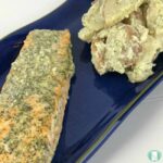 salmon with dill sauce next to potato salad on a plate