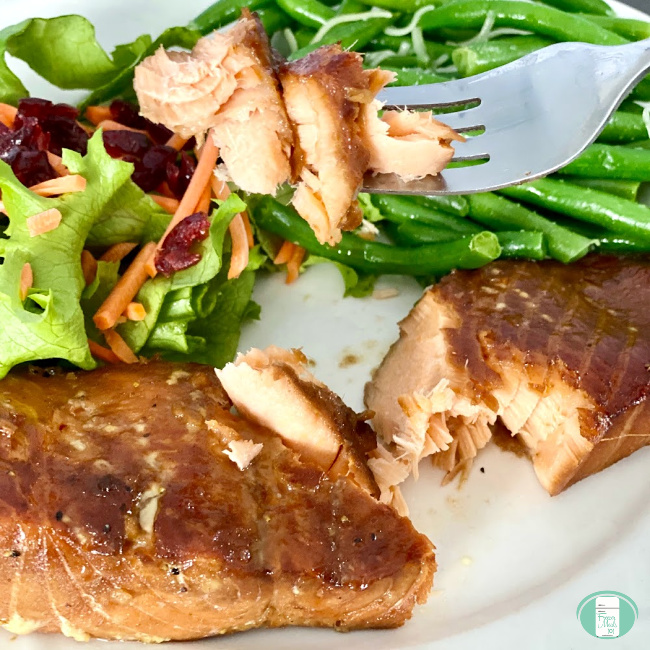 salmon being lifted with a fork off a plate with salmon, green beans, and salad