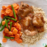 chicken with sauce on rice next to sliced carrots and green beans