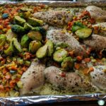 chicken, Brussels sprouts, carrots, zucchini, and corn on a baking sheet