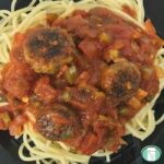 spaghetti pasta topped with red chunky sauce with sausage meatballs