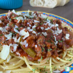 spaghetti noodles topped with meat sauce sprinkled with Parmesan cheese