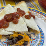 two triangle folded flour tortillas filled with black beans and shredded orange sweet potato topped with salsa