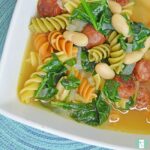 bowl of rotini noodles, beans, sausage slices, and spinach soup