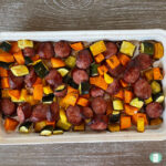 white tray with sliced sausage rounds, cubed sweet potato, cubed zucchini, and cubed butternut squash