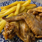 glazed chicken wings next to French fries on a plate