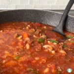 skillet with ground beef, macaroni, and diced vegetables in a simmering red sauce