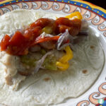 flour tortilla topped with sliced bell peppers, chicken, sliced purple onions, and salsa