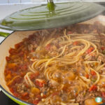 spaghetti noodles in a boiling meat sauce in a skillet