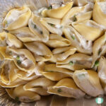 large pasta shells filled with white sauce, cubed chicken, and peas