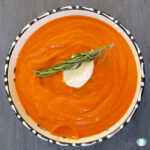 bowl of orange soup topped with a dollop of sour cream and a sprig of rosemary
