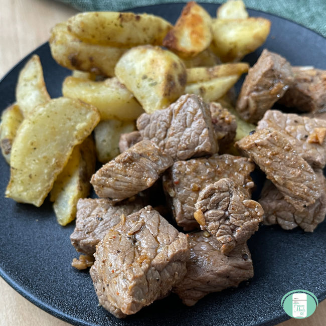 cubes of steak on a plate next to potato wedges