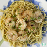 bed of spaghetti noodles on a plate topped with cooked shrimp and fresh herbs