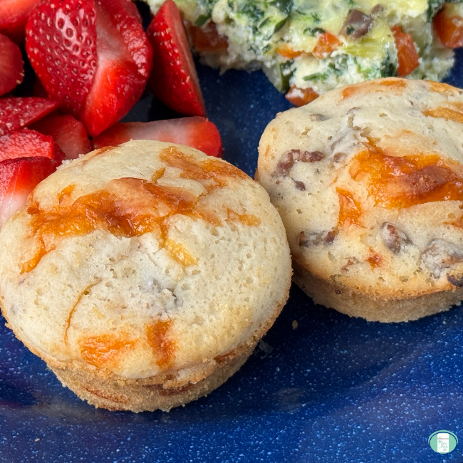 two Sausage breakfast muffins served on a plate with some frittata and sliced fruit