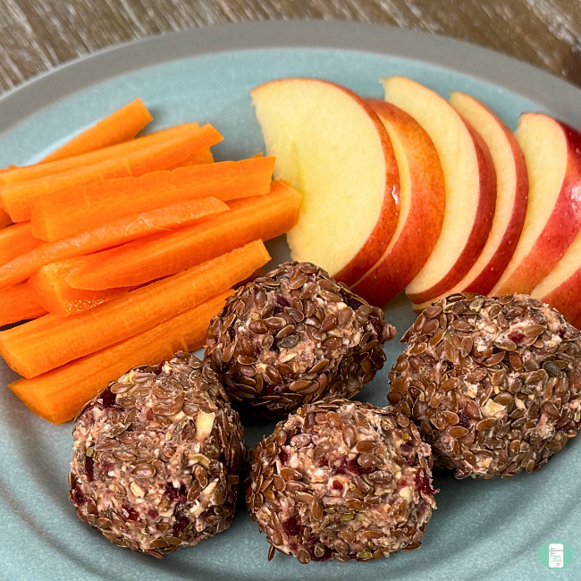 four apple cinnamon energy balls plated with apple slices and carrot sticks