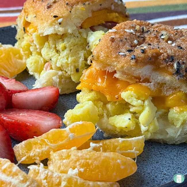 Buns loaded with cheesy scrambled eggs, topped with everything bagel seasoning, served with sliced strawberries and orange segments